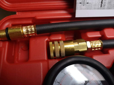 Close-up of brass fittings on a cylinder leak-down tester kit with a black hose and partial gauge in a red case.