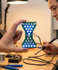Person demonstrating Electronic Hourglass LED DIY Kit For Welding Practice, Blue Ray PCB Board Project, step-by-step guide visible.