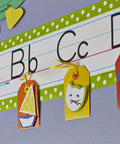 Classroom wall showing removable poster tape with dispenser, holding colorful tags under an alphabet line decoration