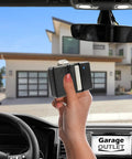 Hand holding Plug And Play Universal Garage Door Opener Remote Compatible With Genie Overhead Door GT90-1 G220 MAT90 GT912 AT90 against garage view