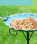 34 Inch Tall Metal Bird Bath On A Stake For Outdoors filled with bird seed, featuring a blue bird design and stable three prong base.