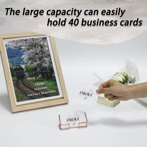 Rose Gold Metal Card Holder For Desk with hand placing card, beside framed photo and text 'The large capacity can easily hold 40 business cards'