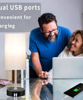 Smart RGB LED Bedside Lamp With USB Charging Ports on table next to smiling couple using laptop, showcasing lamp's USB ports.