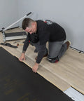 Man kneeling and installing laminate flooring over black Straight Shooter Floor Underlayment For Laminate And Engineered Wood.