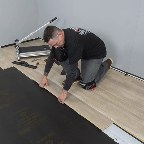 Man kneeling and installing laminate flooring over black Straight Shooter Floor Underlayment For Laminate And Engineered Wood.