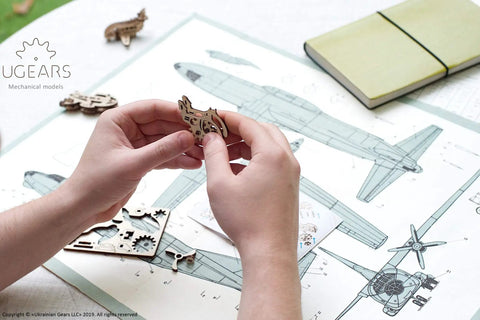 Hands assembling piece from Four Pack Wooden 3D Aircraft Puzzle Kit For Kids 5 Plus Buildable Mechanical Models Helicopter And Hydroplane Style Planes Dope STEM Toy Educational Easy Assembly Natural Wood.