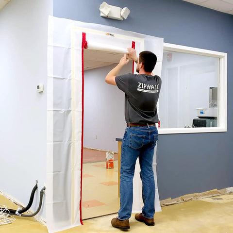Person installing Red ZipDoor Kit For Dust Protection In Remodeling Jobs Pro Grade Flame Retardant Plastic Door Cover With Preinstalled Zippers Easy Access Barrier 4 Mil Thick Heavy Duty Commercial Grade 1 Pack on doorway.