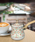 Stainless Steel Turkish Coffee Pot And Milk Warmer With Long Wooden Handle, Red Pattern, 550ml, next to coffee cup in kitchen setting.