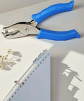 Blue One Circle Hole Punch With Soft Grip Handheld Paper Punch for Crafting next to punched notebook on a white desk.