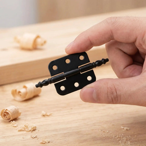 Hand holding Vintage Black Iron Hinges Set For Wooden Boxes And Jewelry Chests, on wooden surface with shavings