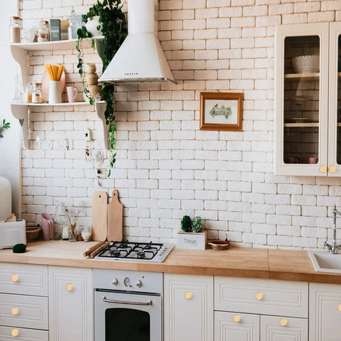 Gold Cabinet Knobs 25 Pack for Dresser and Furniture installed on white kitchen cabinets against brick wall.
