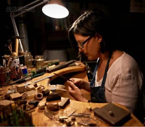 Person crafting jewelry using long needle nose pliers in a dimly lit workspace.