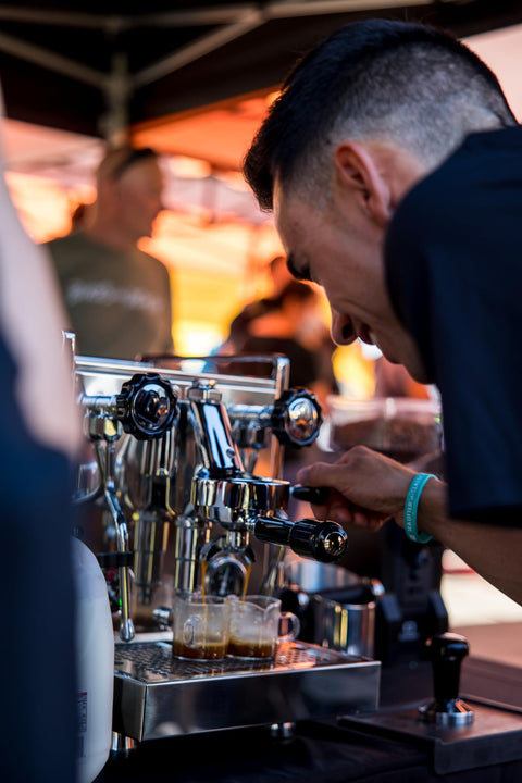 Barista preparing espresso drinks with a commercial coffee machine at an outdoor event