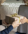 Person giving a wrapped gift box labeled 'Coffee Enthusiast's Milk Frother', for Barista Grade Milk Frother With Variable Temperature And Froth Thickness For Lattes And Hot Chocolate 21 Oz Capacity With Smart Touch Control Dishwasher Safe And Memory Function