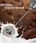 Handheld Milk Frother With Stand, Electric Foam Maker With Stainless Steel Whisk splashing in milk, gray finish visible, high torque motor.