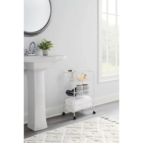 White three tier wheeled wire shelving cart with adjustable metal shelves in bathroom, featuring towels and toiletries, compact design.