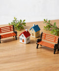 Two Pack 1 To 30 Scale Miniature Park Benches, In Classic Brown And Black Painted Finish, Realistic Tiny Garden Seats For Dollhouses, Model Train Layouts, And Outdoor Scene Decor, shown in a diorama setting with small houses and foliage.