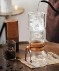 Top Shelf Cold Brew Drip Tower and Ice Drip Coffee Machine pouring water over ice, 400ml glass carafe and wooden base on table.