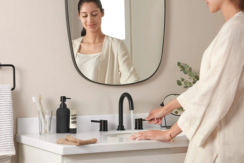 Woman using Precept Widespread Matte Black Bathroom Faucet For 3-Hole 6-16 In. Install With ADA Push Pop-Up Drain