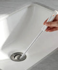 Flexible Drain Snake Cleaner Brush That Kicks Out Greasy Gunk Reusable Spiral Hair Removal Tool With Comfort Grip Handles For Sinks Showers And Bathtubs In White in use in a sink with a hand holding it.