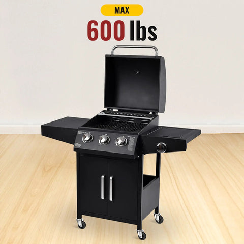 Black 3-burner outdoor grill with open lid and four caster wheels, max 600 lbs capacity displayed on hardwood floor