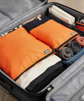 Open suitcase showing three pack travel toiletry bags for men carry-on organizer pouch set zippered cosmetic and electronics pouches orange