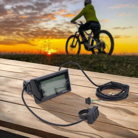 Versatile LCD Display Meter Panel For Electric Bikes And Ebikes Ride Ready With Temperature Speed Time And Power Readouts 24V To 60V Compatibility 5 Pin Connector Easy Install Controller Panel For Scooters And Bikes, displayed on a wooden table with a sunset cycling scene in the background.