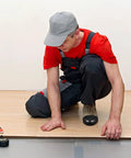 Man wearing Rugged Steel Toe Covers For Boots And Shoes, Tough-As-Nails Toe Caps, in construction setting, kneeling on wooden floor.