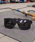 Premium Heavy Duty Industrial Double Lens Welding Goggles Featuring Top Shelf Anti Glare Optics resting on textured floor.