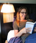 Woman reading in bed under Over The Bed Reading Lamp With Soft Cream Pleated Fabric Shade And No Fuss Easy On Off Pull Cord Eye Friendly Bedside Light Great For Reading Knitting Puzzles And Late Night Chats In Bed Mounts Above The Headboard.