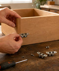 Person installing metal brackets on a wooden drawer using a screwdriver, with screws visible on a workbench.