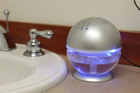 Little Squirt Glowing Water Air Revitalizer And Diffuser With 10ml Lavender Oil emitting blue light, placed on bathroom counter.