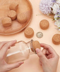 Person placing 8 Pack Wooden Cork Stoppers for Wide Mouth Bottles 1 to 2 Inch Opening on glass bottle, with wooden lid detail.
