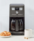 14 Cup PerfecTemp Programmable Coffee Maker With Glass Carafe And 1 4 Cup Setting Brew Strength Control Brew Pause And Over Ice Function In Black Stainless Steel on kitchen counter with cup of coffee