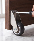 Installing a 2 Pack Low Profile Anti Sag Caster Wheel on furniture with a screwdriver for smooth movement.