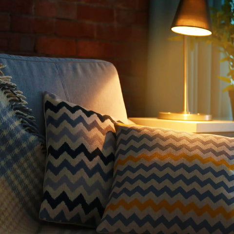 Cozy living room scene with a lamp illuminating patterned cushions on a sofa, showcasing warm lighting ambiance.