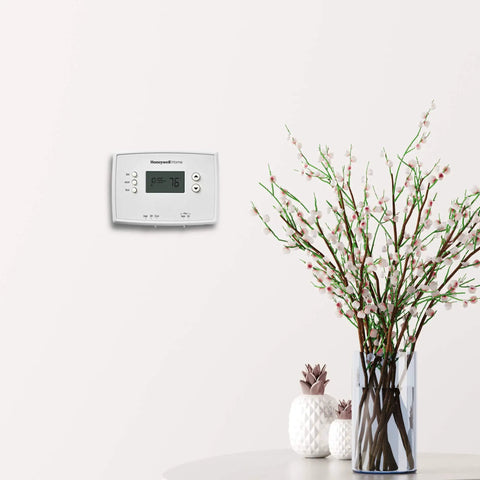 Programmable Thermostat With One Week Programming And Digital Display White mounted on wall beside vase with branches
