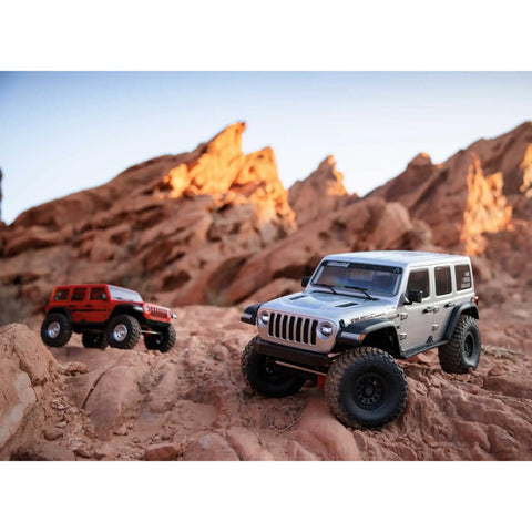 Two One Sixth Scale SCX6 Jeep Wrangler 4x4 Rock Crawler RTRs with two speed transmission on rocky terrain, silver and red models