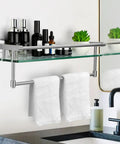 Brushed Nickel 20 Inch Glass Bathroom Shelf With Towel Bar, holding toiletries, mounted above a sink near a mirror.