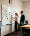 Two people at a whiteboard in an office, planning with notes, clocks on wall
