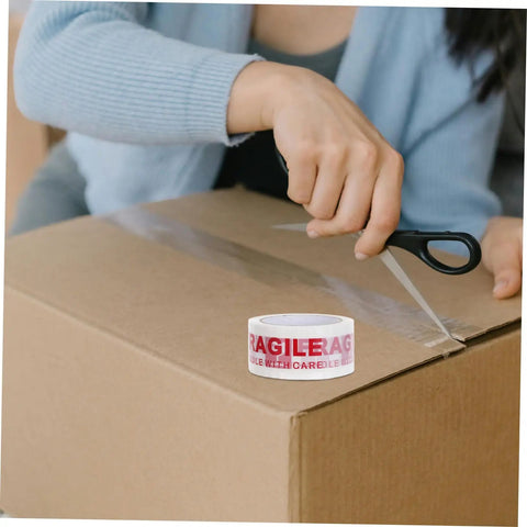 Person using Fragile Warning Packing Tape Set with 5 rolls to seal a cardboard box; heavy duty shipping tape for safe parcel handling.