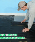 Person installing Heavy Duty Black Underlayment Roll With Adhesive Strip For Vinyl Laminate Engineered Wood Floors 6 Mil thick over concrete subfloor.