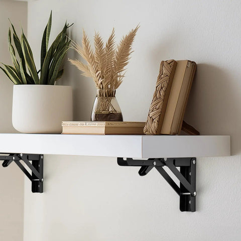 Super Sturdy Matte Black Folding Shelf Brackets To Clear Your Clutter Fast These Compact Fold Down Wall Mount Supports Rock In Tight Spots Perfect For Garages Shops Or Kitchens Zero Sweat Two Pack, supporting a white shelf with decor.