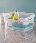 Solid As A Rock Clear Storage Bins Three Pack Tough As Nails Transparent Plastic Crates Built For Closet Shelf And Garage Organizing Zero Fuss Setup Measuring 14 By 11 By 7 Inches filled with towels and cleaning supplies on a counter.