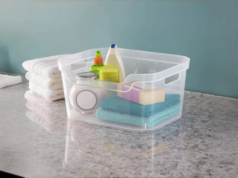 Solid As A Rock Clear Storage Bins Three Pack Tough As Nails Transparent Plastic Crates Built For Closet Shelf And Garage Organizing Zero Fuss Setup Measuring 14 By 11 By 7 Inches filled with towels and cleaning supplies on a counter.