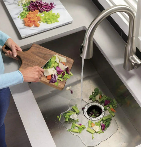 Disposall Garbage Disposal With Continuous Feed 0.5 HP Motor in kitchen sink grinding vegetables, water running from faucet