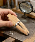 Hand holding Wooden Ring Clamp With Leather Jaws And Dope Wedge Lock for engraving rings on workbench with tools.