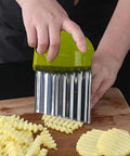 Close-up of green-handled crinkle cutter with stainless steel ribbed blade held over potatoes on a wooden cutting board