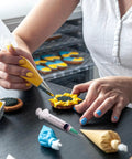 Person decorating cookies with precision glue syringe and piping bag, highlighting the product's application in delicate craft projects.