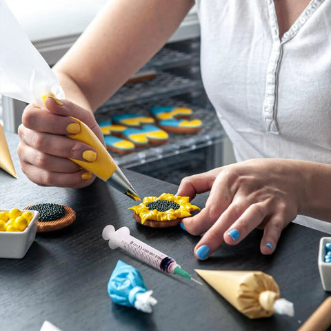 Person decorating cookies with precision glue syringe and piping bag, highlighting the product's application in delicate craft projects.